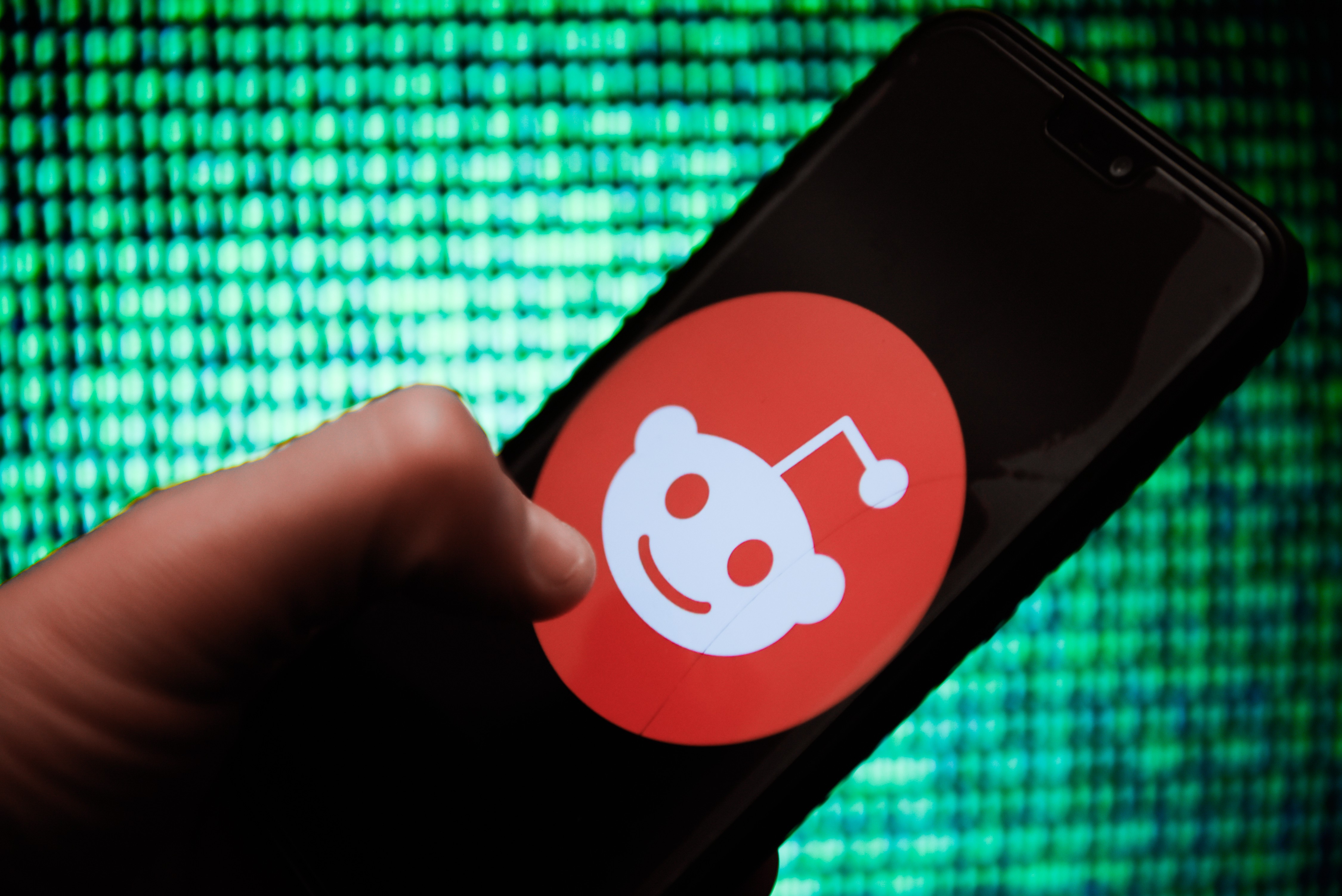 In this photo illustration, a hand holds up an Android mobile phone displaying the Reddit logo.