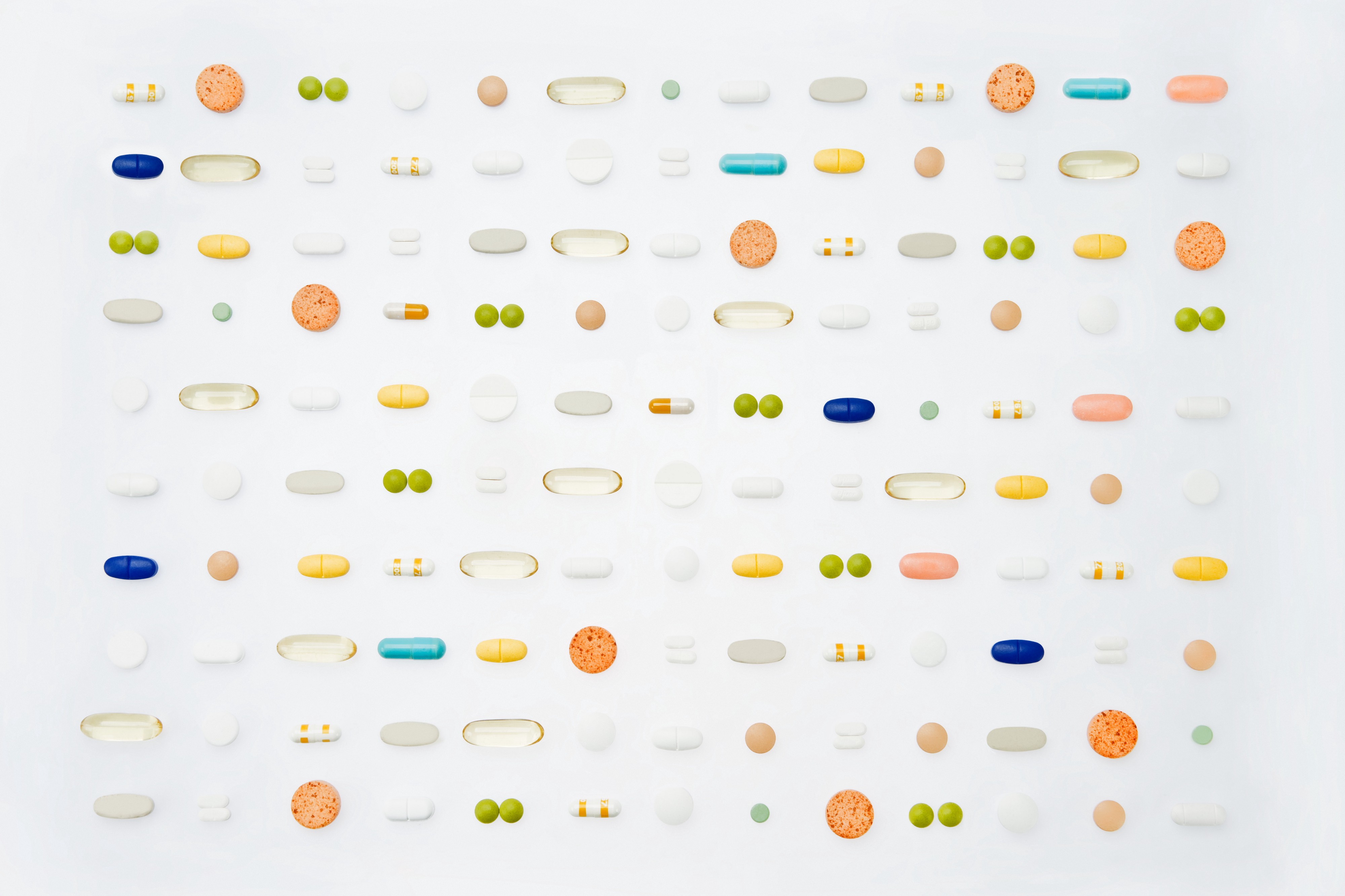 A variety of different pills and supplements are laid out in a grid against a white backdrop.