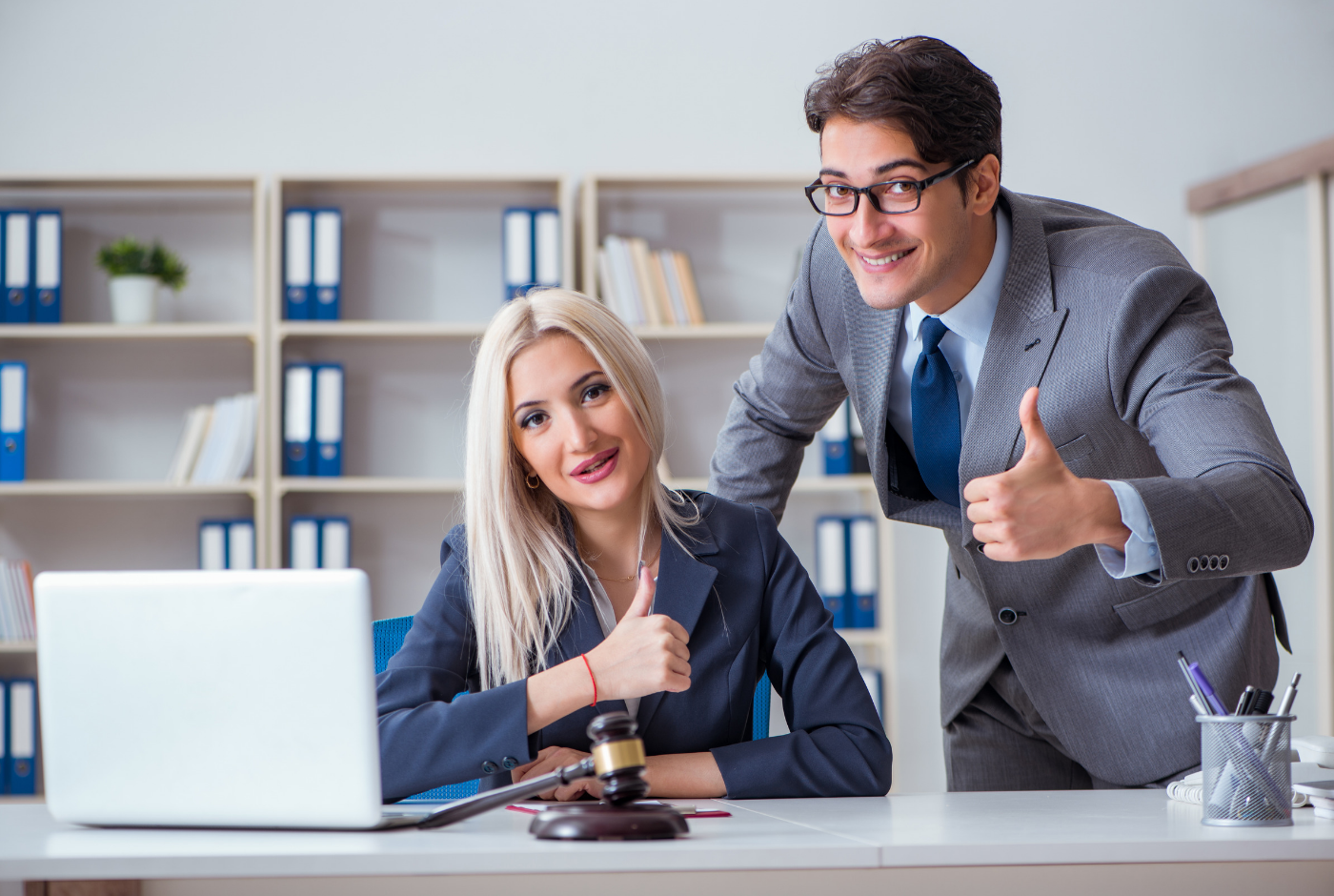 Professional man and woman in business suits with fake smiles at desk with laptop and gavel on it.